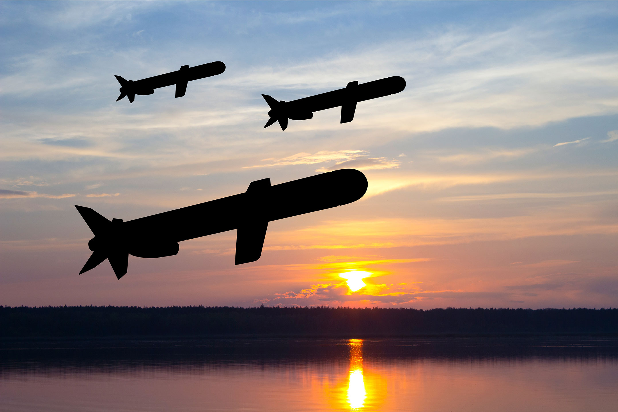 Silhouettes of three tomahawk cruise missiles in the sky against the sunset